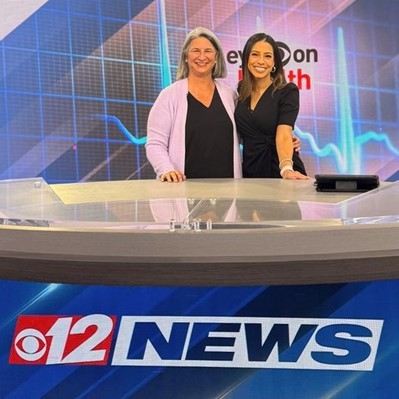 Two women standing in front of a news desk
Description automatically generated